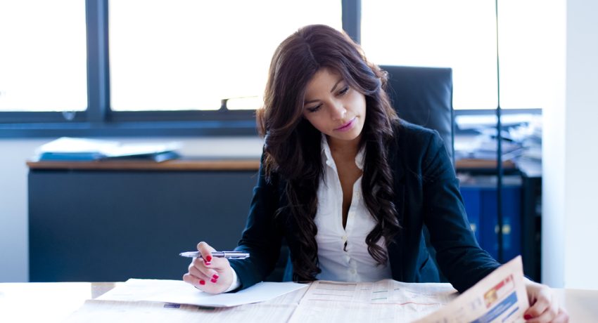 young real estate agent reads newspaper on her desk