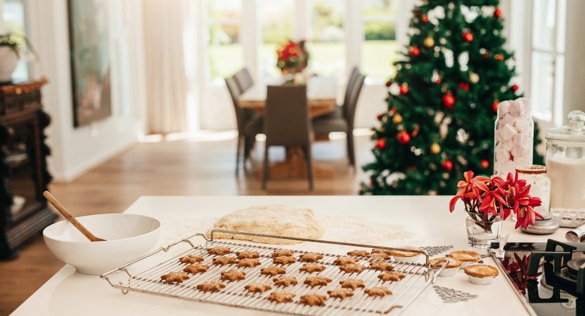 Tray of baked star cookies and dough placed on kitchen table. Decorated Christmas tree in the background.